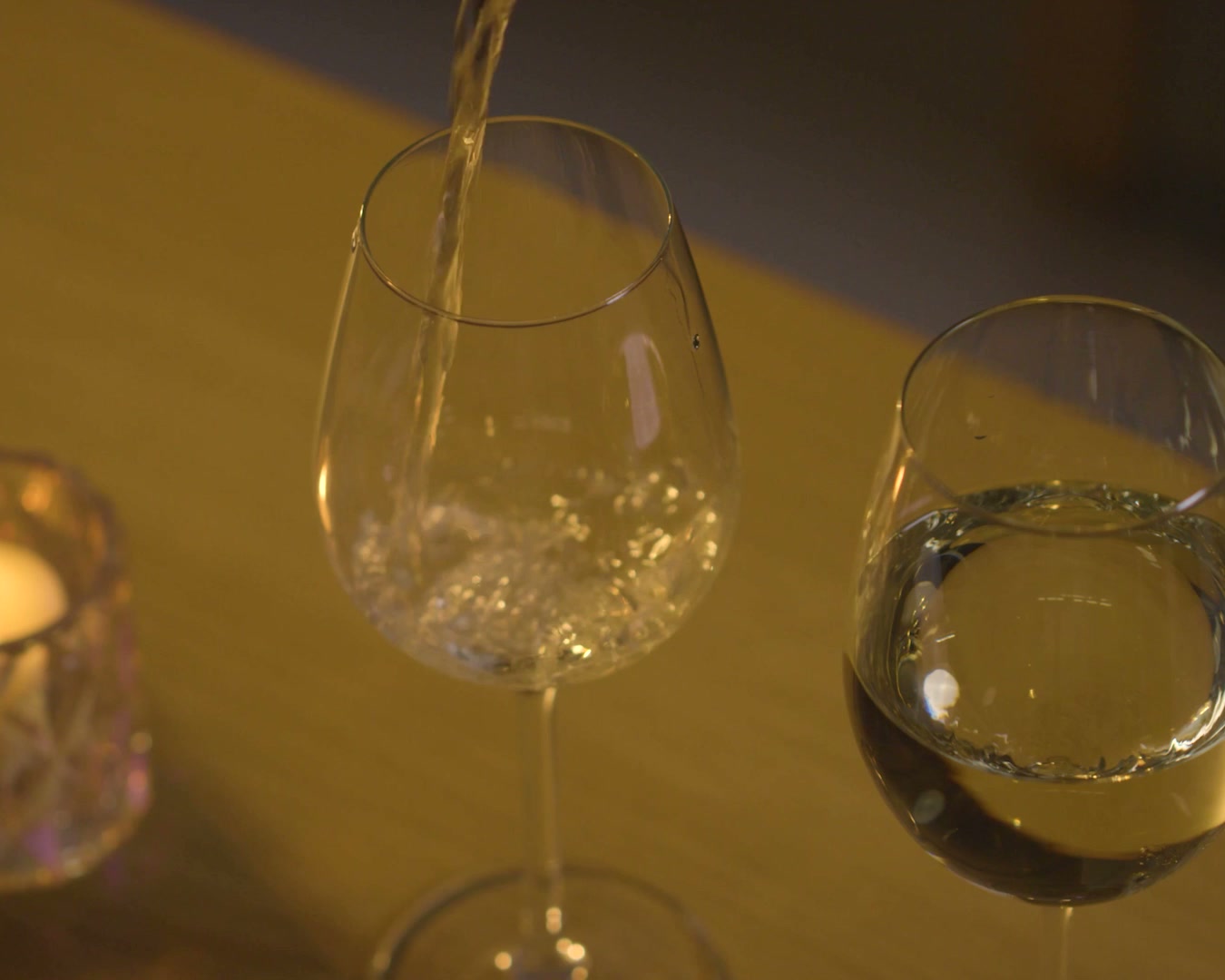 White wine being poured into a glass under warm directional lighting.